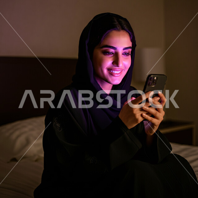 التسوق الإلكتروني عبر التطبيقات، بورتريه مقرب لسيدة عربية خليجية سعودية محجبة مبتسمة  تحمل بيدها الهاتف المحمول، قضاء اوقات ممتعة بتبادل الاخبار والأحاديث, التواصل والاطمئنان على الأصدقاء, تعابير الفرح عند سماع الاخبار السارة