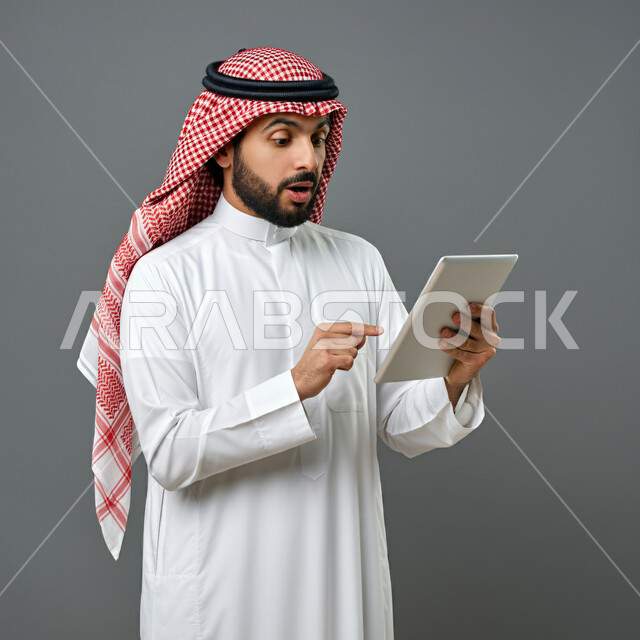 Gestures indicating focus on achieving company goals, Saudi companies and jobs, completing work tasks using a tablet, working in a comfortable environment, the concept of integrating work with technology and technology, portrait of a Gulf man wearing a Saudi thobe, gray background