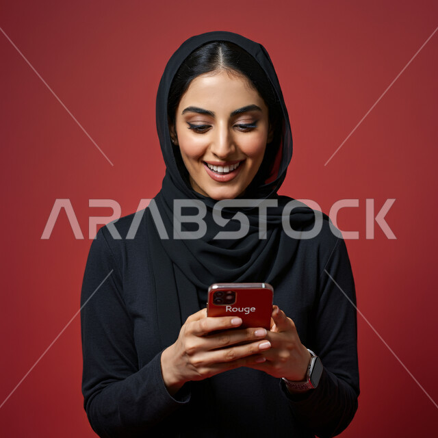 التسوق الإلكتروني عبر التطبيقات، بورتريه مقرب لسيدة عربية خليجية سعودية محجبة مبتسمة تحمل بيدها الهاتف المحمول، قضاء اوقات ممتعة بتبادل الاخبار والأحاديث, التواصل والاطمئنان على الأصدقاء, تعابير الفرح عند سماع الاخبار السارة