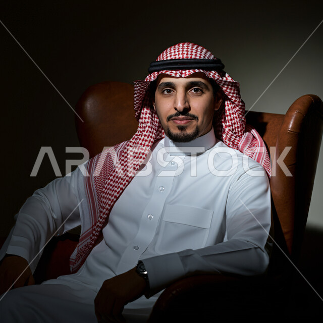 مفهوم الهيبة والرجولة، الاناقة والاهتمام بالمظهر الخارجي, بورتريه مقرب لرجل عربي خليجي سعودي يرتدي الزي الشعبي التقليدي ينظر الى الكميرا بتعابير السرور و الثقة بالنفس، خلفية سوداء 