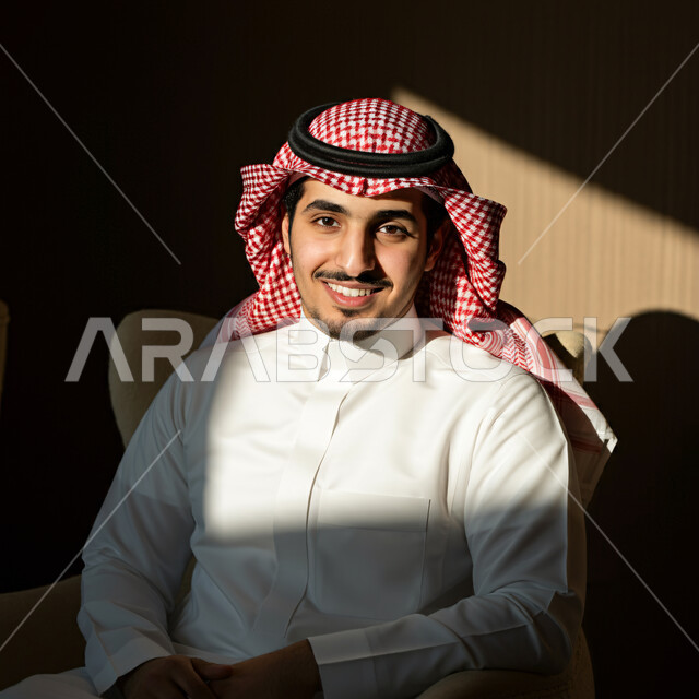 The concept of prestige and masculinity, elegance and interest in external appearance, close-up portrait of a Saudi Arabian Gulf man wearing traditional folk costume looking at the camera with expressions of pleasure and self-confidence, black background