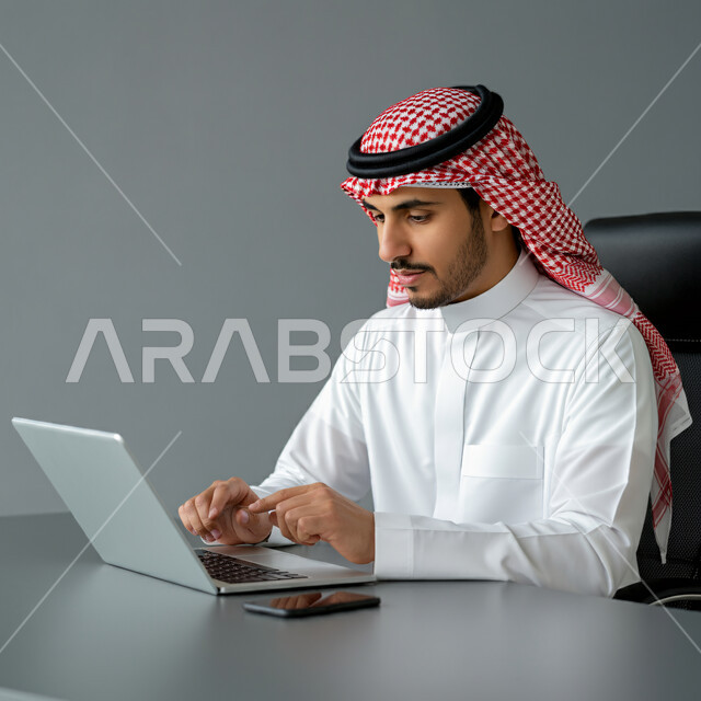 ادارة مهام العمل اليومية في مقر الشركة، مهن ووظائف سعودية، استخدام الاجهزة التقنية الحديثة، رجل عربي خليجي سعودي يرتدي الزي التقليدي يجلس في مكتبه يعمل على جهاز الحاسوب المحمول، تطوير خطط وآليه العمل, مهن ووظائف سعودية, دمج العمل مع التقنية والتكنولوجيا