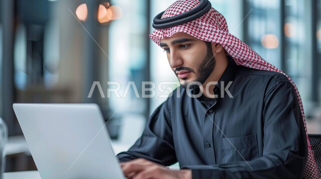 دمج العمل مع التقنيات والتكنولوجيا، مهن ووظائف ادارية مكتبية, إنجاز المهام العمل المطلوبة ، مفهوم إدارة شؤون الأعمال وتنظيمها عبر الاجهزة التقنية، رجل اعمال عربي خليجي سعودي يرتدي الثوب التقليدي والشماغ يعمل على الحاسوب المحمول، ايماءات الاندماج والتركيز