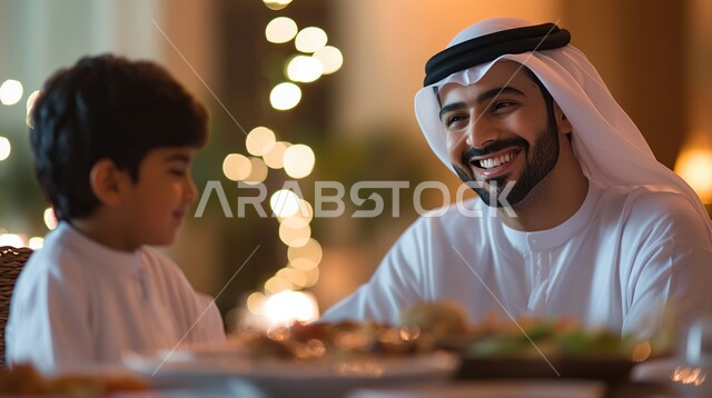 قضاء أوقات ممتعة مع الاسرة في المنزل، مائدة الطعام المليئة بأصناف المأكولات الشهية، ايماءات السعادة والسرور، أجواء عائلية مليئة بالحب، صورة مقربة لاب عربي خليجي سعودي يجلس حول السفرة برفقة ولده