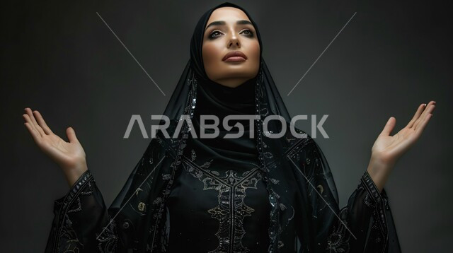 التضرع و طلب العون والحمد والشكر، العباده والتقرب الى الله، بورتريه مقرب لإمرأة مسلمة عربية خليجية سعودية ترتدي العباءة السوداء المطرزة والحجاب ترفع يديها للدعاء، خلفية سوداء 