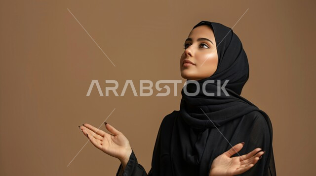الحمد والشكر والتضرع و طلب العون، العباده والتقرب الى الله، بورتريه مقرب من الجانب لإمرأة مسلمة عربية خليجية سعودية ترتدي العباءة السوداء والحجاب ترفع يديها للدعاء، خلفية بيج