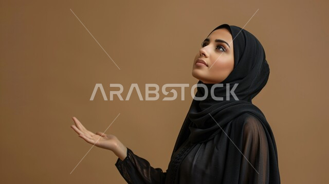 الحمد والشكر والتضرع و طلب العون، العباده والتقرب الى الله، بورتريه مقرب من الجانب لإمرأة مسلمة عربية خليجية سعودية ترتدي العباءة السوداء والحجاب ترفع يديها للدعاء، خلفية بيج