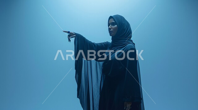 Accusation, blaming, reprimand, request to stop doing wrong, pointing out something, annoyance and desire for revenge, close-up portrait of a Saudi Arabian Gulf woman wearing a black abaya raising index finger to point out someone (you), blue background