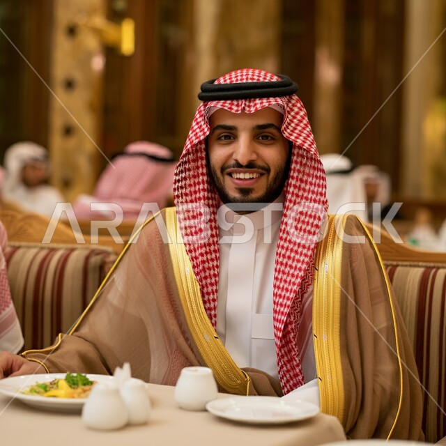 قضاء أوقات ممتعة في المطعم, مطاعم و كافيهات المملكة العربية السعودية, الاستمتاع بالغداء في الخارج, شاب عربي خليجي سعودي مبتسم يرتدي الثوب التقليدي و الشماغ يجلس على المائدة و يقوم بتناول الطعام, النظر إلى الكاميرا بإيماءات السعادة و السرور