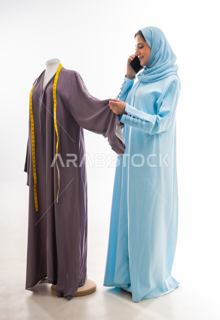 التواصل مع الأهل والأصدقاء أثناء العمل، اختراع وابتكار موديلات جديدة وعصرية، بورتريه لمصممة عربية خليجية عمانية ترتدي عباءة زرقاء تقوم بإجراء مكالمة، ورشة عمل تصميم ازياء، مهن وأعمال فنية نسائية، فنون ومهارات تفصيل الملابس النسائية، مفهوم عالم الأزياء والموضة