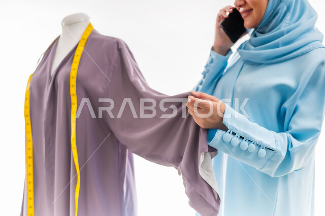 Communicating with family and friends while working, inventing and creating new and modern models, portrait of an Arab Gulf Omani designer wearing a blue abaya making a call, fashion design workshop, women's professions and artistic works, arts and skills of tailoring women's clothing, concept of the world of fashion and style