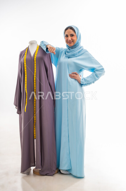 The concept of the world of fashion and style, invention and innovation of new and modern models, portrait of an Omani designer standing next to a model looking with gestures of joy and happiness, the importance of women in the field of sewing, fashion design workshop, women's professions and artistic works, arts and skills of tailoring women's clothing
