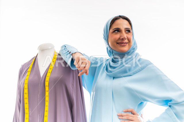 The concept of the world of fashion and style, invention and innovation of new and modern models, portrait of an Omani designer standing next to a model looking with gestures of joy and happiness, the importance of women in the field of sewing, fashion design workshop, women's professions and artistic works, arts and skills of tailoring women's clothing
