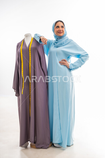 The concept of the world of fashion and style, invention and innovation of new and modern models, portrait of an Omani designer standing next to a model looking with gestures of joy and happiness, the importance of women in the field of sewing, fashion design workshop, women's professions and artistic works, arts and skills of tailoring women's clothing