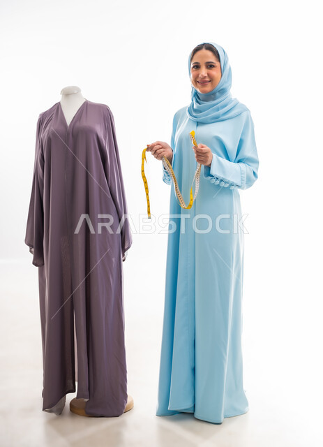 Inventing and innovating new and modern designs, portrait of an Omani designer holding a metric tape in her hand forming the letter N in English, the importance of women in the field of sewing, fashion design workshop, women’s professions and artistic works, arts and skills of tailoring women’s clothing, the concept of the world of fashion and style