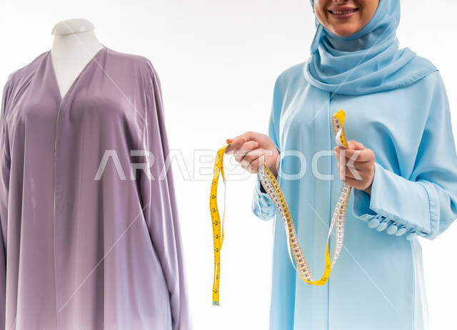 اختراع وابتكار تصاميم جديدة وعصرية، بورتريه لمصممة عمانية تحمل بيدها شريط متري يشكل حرف إن بالإنجليزي، أهمية المرأة في مجال الخياطة، ورشة عمل تصميم ازياء، مهن وأعمال فنية نسائية، فنون ومهارات تفصيل الملابس النسائية، مفهوم عالم الأزياء والموضة