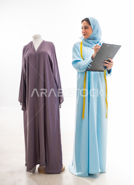 تدوين ورسم الموديلات، اختراع وابتكار موديلات جديدة وعصرية، بورتريه لمصممة عمانية تحمل ورقة وقلم تقوم بتسجيل القياسات، أهمية المرأة في مجال الخياطة، ورشة عمل تصميم ازياء، مهن وأعمال فنية نسائية، فنون ومهارات تفصيل الملابس النسائية، مفهوم عالم الأزياء والموضة