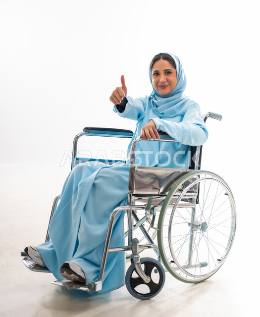 The concept of optimism and love of life, caring for people with disabilities and providing for their needs, a portrait of a smiling Gulf Arab Omani woman wearing a hijab and an abaya with special needs sitting in a wheelchair, providing devices and equipment that help with movement and mobility, white background