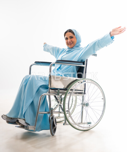 مفهوم التفاؤل وحب الحياة، العنايه بأصحاب الهمم وتأمين احتياجاتهم، بورتريه لإمرأة  عربية خليجية عمانية مبتسمة ترتدي الحجاب والعباءة من ذوي الاحتياجات الخاصه تجلس على كرسي متحرك، توفير اجهزة ومعدات تساعد بالحركة والتنقل، خلفيه بيضاء