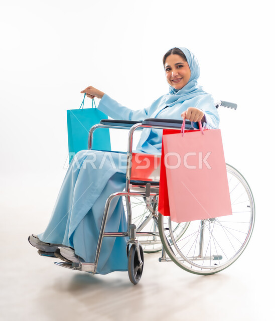 مفهوم التفاؤل وحب الحياة، العنايه بأصحاب الهمم وتأمين احتياجاتهم، بورتريه لإمرأة  عربية خليجية عمانية مبتسمة ترتدي الحجاب والعباءة من ذوي الاحتياجات الخاصه تجلس على كرسي متحرك، توفير اجهزة ومعدات تساعد بالحركة والتنقل، خلفيه بيضاء