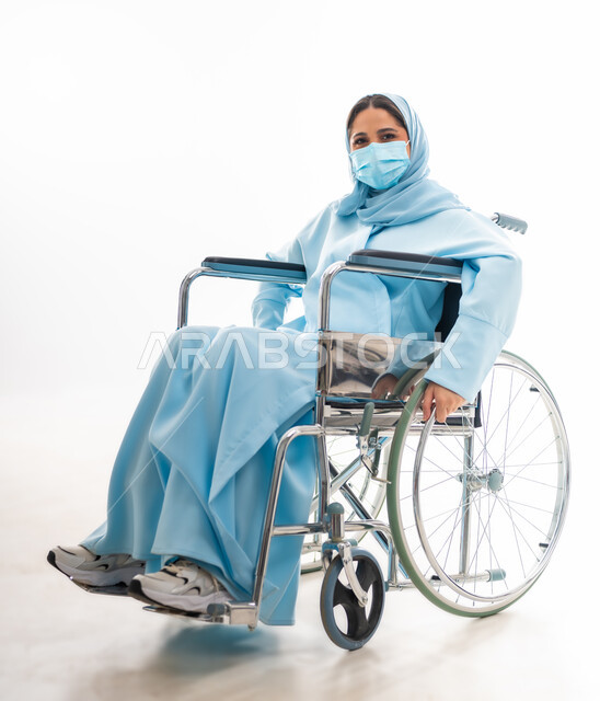 مفهوم التفاؤل وحب الحياة، العنايه بأصحاب الهمم وتأمين احتياجاتهم، بورتريه لإمرأة  عربية خليجية عمانية مبتسمة ترتدي الحجاب والعباءة من ذوي الاحتياجات الخاصه تجلس على كرسي متحرك، توفير اجهزة ومعدات تساعد بالحركة والتنقل، خلفيه بيضاء