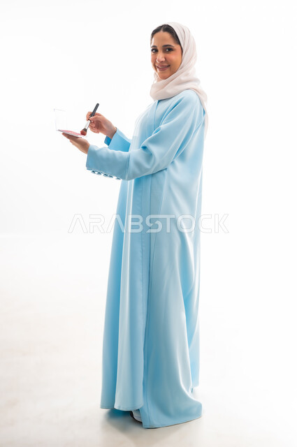 الأنوثة والاهتمام بالجمال والبشرة والمظهر الخارجي, مفهوم الدعاية والإعلان، خبيرة لمستحضرات التجميل النسائية، بورتريه لإمرأة عربية خليجية عمانية ترتدي العباءة والحجاب تقوم بوضع أحمر الخدود، التسويق لمنتجات الميك اب، خلفية بيضاء