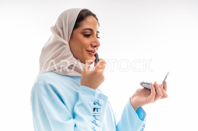 التسويق لمنتجات الميك اب، مفهوم الأنوثة والاهتمام بالجمال والبشرة والمظهر الخارجي, خبيرة لمستحضرات التجميل النسائية، بورتريه لإمرأة عربية خليجية عمانية ترتدي العباءة والحجاب تقوم بوضع أحمر الشفاه، خلفية بيضاء