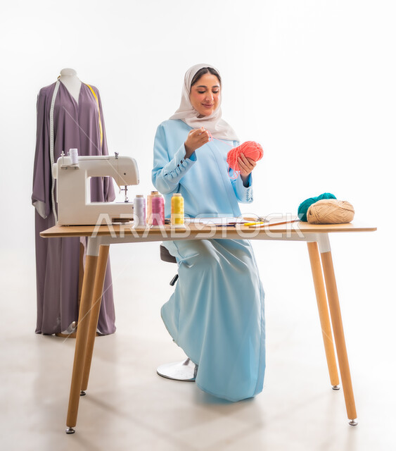 The importance of women in the field of sewing, invention and innovation of new and modern models, portrait of an Arab Gulf Omani woman wearing a blue abaya holding a ball of woolen thread in her hand, fashion design workshop, women's professions and artistic works, arts and skills of tailoring women's clothing, concept of the world of fashion and style
