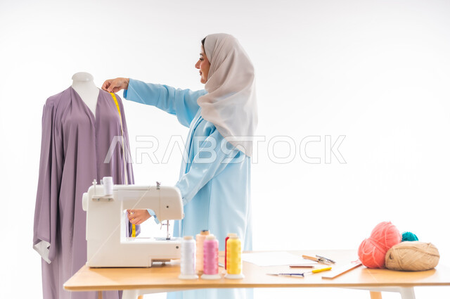 اختراع وابتكار تصاميم جديدة وعصرية، بورتريه لمرأة عربيه خليجيه عمانية ترتدي عباءة زرقاء تقوم بأخذ مقاسات ثوب،  أهمية المرأة في مجال الخياطة، ورشة عمل تصميم ازياء، مهن وأعمال فنية نسائية، فنون ومهارات تفصيل الملابس النسائية، مفهوم عالم الأزياء والموضة
