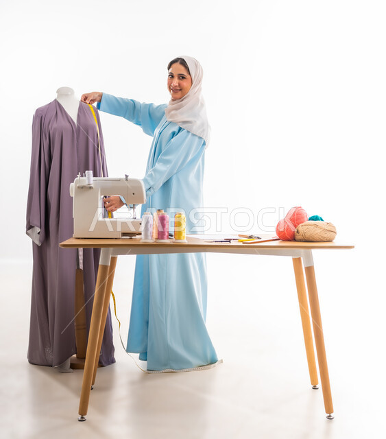 النظر للكاميرا بايماءات الفرح، اختراع وابتكار موديلات جديدة وعصرية، بورتريه لمصممة عمانية تقوم بأخذ المقاسات المناسبة،أهمية المرأة في مجال الخياطة، ورشة عمل تصميم ازياء، مهن وأعمال فنية نسائية، فنون ومهارات تفصيل الملابس النسائية، مفهوم عالم الأزياء والموضة