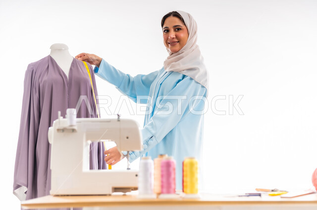 النظر للكاميرا بايماءات الفرح، اختراع وابتكار موديلات جديدة وعصرية، بورتريه لمصممة عمانية تقوم بأخذ المقاسات المناسبة،أهمية المرأة في مجال الخياطة، ورشة عمل تصميم ازياء، مهن وأعمال فنية نسائية، فنون ومهارات تفصيل الملابس النسائية، مفهوم عالم الأزياء والموضة