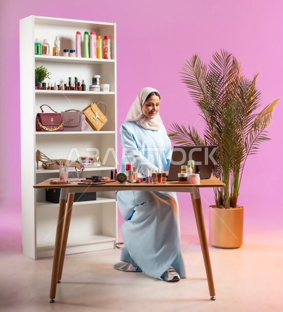 استخدام التقنيات الحديثة في مجال الميك اب، إمرأة عربية عمانية ترتدي عباءة زرقاء تجلس على كرسي وتقوم بالعمل على الحاسب المحمول، مفهوم الانوثه والاهتمام بالمظهر الخارجي, أدوات تجميل نسائيه عصريه، التسويق لمنتجات التجميل, مكياج وميكاب تتوريال, صالون نسائي راقي