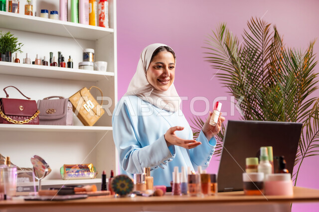 أهمية التسويق لمنتجات التجميل عبر منصات التواصل الاجتماعي, مفهوم الانوثه والاهتمام بالمظهر الخارجي, إمرأة عربية خليجية عمانية ترتدي عباءة زرقاء تجلس أمام الحاسوب المحمول وتقوم بعرض منتج تجميلي، أدوات تجميل نسائيه عصريه، مكياج وميكاب تتوريال, صالون نسائي راقي