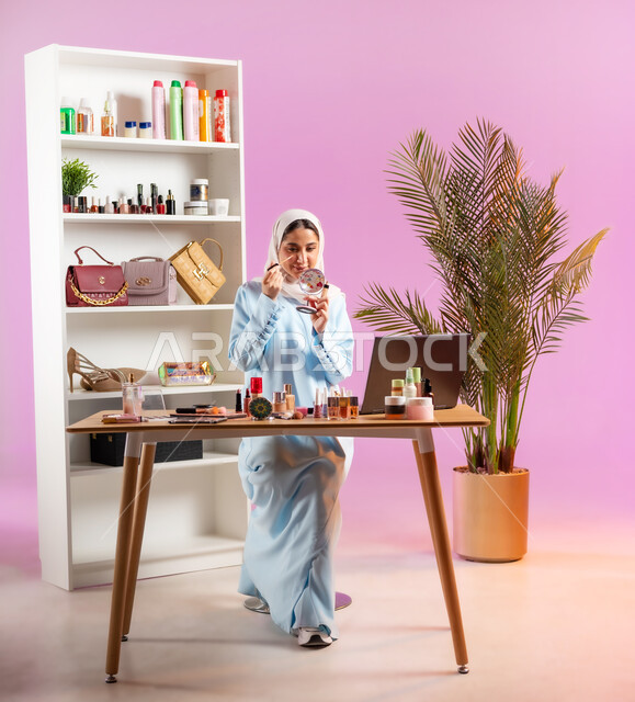 مكياج وميكاب تتوريال, مفهوم الانوثه والاهتمام بالمظهر الخارجي, إمرأة عربية خليجية عمانية محجبة ترتدي عباءة زرقاء تقوم بوضع احد مساحيق الميك اب، أدوات تجميل نسائيه عصريه، التسويق لمنتجات التجميل, صالون نسائي راقي