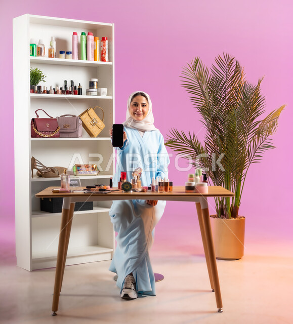 Using modern and advanced devices for marketing purposes, an Omani Gulf woman looks at the camera with smiling gestures, displaying a blank black screen, femininity and interest in external appearance, modern women's cosmetics, marketing for beauty products, makeup and makeup tutorial, upscale women's salon