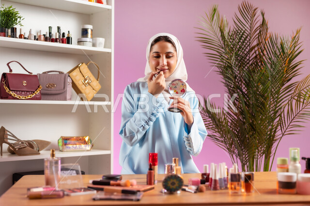 أزياء واكسسوارات نسائية عصريه، إمرأة عربية خليجية عمانية محجبة ترتدي عباءة زرقاء تقوم بوضع أحمر الشفاه، مفهوم الانوثه والاهتمام بالمظهر الخارجي, أدوات تجميل نسائيه عصريه، التسويق لمنتجات التجميل, مكياج وميكاب تتوريال, صالون نسائي راقي