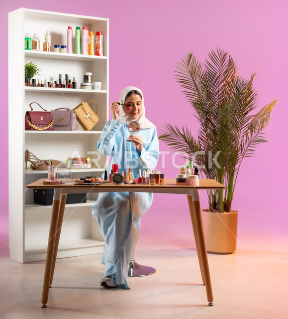 مفهوم الانوثه والاهتمام بالمظهر الخارجي, إمرأة عربية خليجية عمانية محجبة ترتدي عباءة زرقاء تقوم بوضع احد مساحيق الميك اب، أدوات تجميل نسائيه عصريه، التسويق لمنتجات التجميل, مكياج وميكاب تتوريال, صالون نسائي راقي
