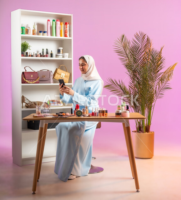 أدوات تجميل نسائيه عصريه، مفهوم الانوثه والاهتمام بالمظهر الخارجي، إمرأة عربية خليجية عمانية محجبة ترتدي عباءة زرقاء تحمل بيدها موبايل، التسويق لمنتجات التجميل, مكياج وميكاب تتوريال, صالون نسائي راقي