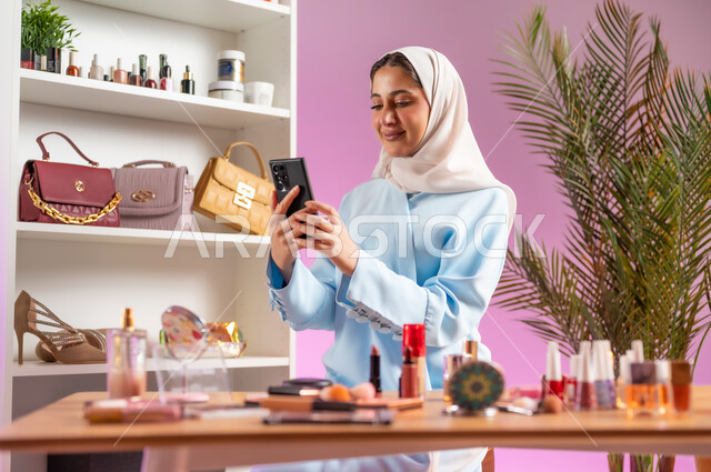 أدوات تجميل نسائيه عصريه، مفهوم الانوثه والاهتمام بالمظهر الخارجي، إمرأة عربية خليجية عمانية محجبة ترتدي عباءة زرقاء تحمل بيدها موبايل، التسويق لمنتجات التجميل, مكياج وميكاب تتوريال, صالون نسائي راقي