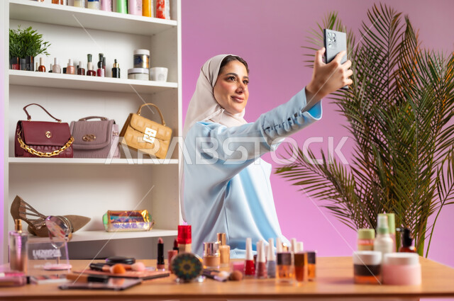 مفهوم الانوثه والاهتمام بالمظهر الخارجي, إمرأة عربية خليجية عمانية محجبة ترتدي عباءة زرقاء تقوم بالتقاط صورة سيلفي، أدوات تجميل نسائيه عصريه، التسويق لمنتجات التجميل, مكياج وميكاب تتوريال, صالون نسائي راقي
