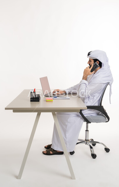 أداء المهام والاعمال المكتبيه داخل مقر الشركه، بورتريه مقرب لرجل عربي خليجي اماراتي يرتدي الكندوره والغتره البيضاء الاماراتيه يجلس خلف المكتب ويقوم بالعمل على جهاز الاب توب المحمول، دراسه المشاريع ومراجعه التقارير السنويه، الاشراف على المخططات وتحليل اداء العمل، جلسه عمل عن بعد، خلفيه بيضاء