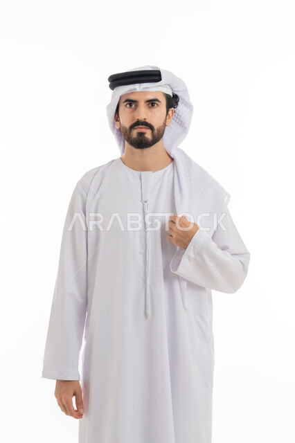 مفهوم الاناقه والرجوله والاهتمام بالمظهر الخارجي، الوقوف باستقامه والنظر الى الكاميرا بايماءات الثقه بالنفس، بورتريه بالطول الكامل لرجل عربي خليجي اماراتي يرتدي الكندوره والغتره البيضاء الاماراتيه يقف بايماءات الرجوله وعزه النفس، خلفيه بيضاء