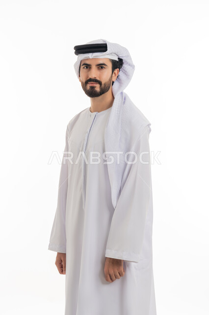 مفهوم الاناقه والرجوله والاهتمام بالمظهر الخارجي، الوقوف باستقامه والنظر الى الكاميرا بايماءات الثقه بالنفس، بورتريه بالطول الكامل لرجل عربي خليجي اماراتي يرتدي الكندوره والغتره البيضاء الاماراتيه يقف بايماءات الرجوله وعزه النفس، خلفيه بيضاء
