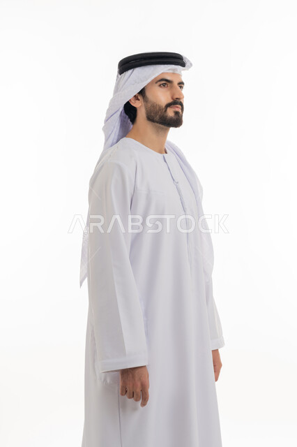 مفهوم الاناقه والرجوله والاهتمام بالمظهر الخارجي، الوقوف باستقامه والنظر الى الكاميرا بايماءات الثقه بالنفس، بورتريه بالطول الكامل لرجل عربي خليجي اماراتي يرتدي الكندوره والغتره البيضاء الاماراتيه يقف بايماءات الرجوله وعزه النفس، خلفيه بيضاء