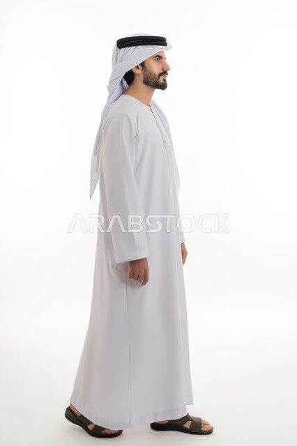 مفهوم الاناقه والرجوله والاهتمام بالمظهر الخارجي، الوقوف باستقامه والنظر الى الكاميرا بايماءات الثقه بالنفس، بورتريه بالطول الكامل لرجل عربي خليجي اماراتي يرتدي الكندوره والغتره البيضاء الاماراتيه يقف بايماءات الرجوله وعزه النفس، خلفيه بيضاء