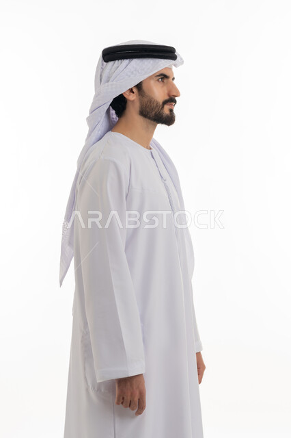 مفهوم الاناقه والرجوله والاهتمام بالمظهر الخارجي، الوقوف باستقامه والنظر الى الكاميرا بايماءات الثقه بالنفس، بورتريه بالطول الكامل لرجل عربي خليجي اماراتي يرتدي الكندوره والغتره البيضاء الاماراتيه يقف بايماءات الرجوله وعزه النفس، خلفيه بيضاء