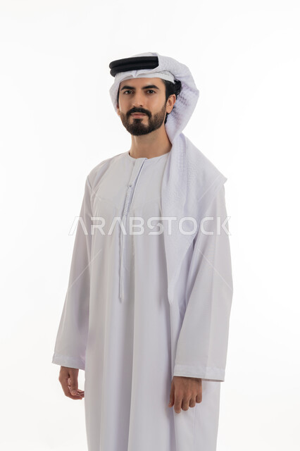 مفهوم الاناقه والرجوله والاهتمام بالمظهر الخارجي، الوقوف باستقامه والنظر الى الكاميرا بايماءات الثقه بالنفس، بورتريه بالطول الكامل لرجل عربي خليجي اماراتي يرتدي الكندوره والغتره البيضاء الاماراتيه يقف بايماءات الرجوله وعزه النفس، خلفيه بيضاء