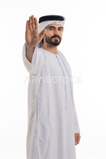 الصمت والتوقف عن فعل شئ ما، الوقوف بغضب ورفض أمر محدد, بوتريه جانبي لشاب عربي خليجي إماراتي يرتدي الكندورة والغترة البيضاء يرفع كفه للأعلى بإيماءات الانزعاج والنهي، طلب عدم التدخل والامتناع عن فعل أمر معين, خلفية بيضاء