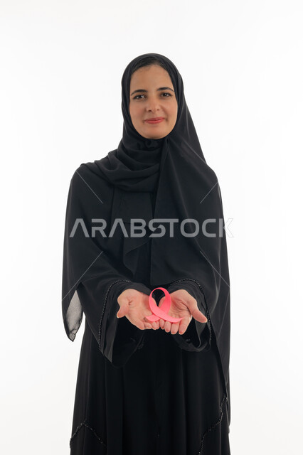 رمز الحملة العالمية لسرطان الثدي، تحدي الأمراض الخبيثة، بورتريه لسيده عربية خليجية إماراتية ترتدي الحجاب والعباءة السوداء تحمل بيديها الشريط الوردي، شابة  تنظر الى الكاميرا بإيماءات البهجة والتفاؤل، حملة نسائية توعوية للكشف المبكر عن سرطان الثدي، خلفية بيضاء