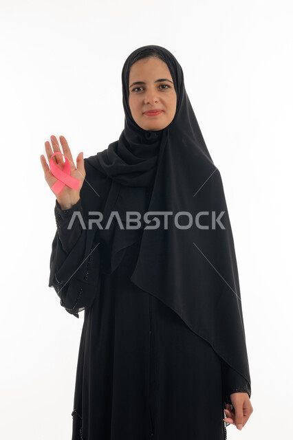 رمز الحملة العالمية لسرطان الثدي، تحدي الأمراض الخبيثة، بورتريه لسيده عربية خليجية إماراتية ترتدي الحجاب والعباءة السوداء تحمل بيديها الشريط الوردي، شابة  تنظر الى الكاميرا بإيماءات البهجة والتفاؤل، حملة نسائية توعوية للكشف المبكر عن سرطان الثدي، خلفية بيضاء